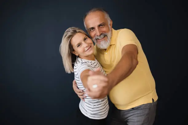 A senior couple, both with serene smiles, dances in a studio shot, highlighting the beauty and vitality of their love, which has only deepened with time and shared experiences.